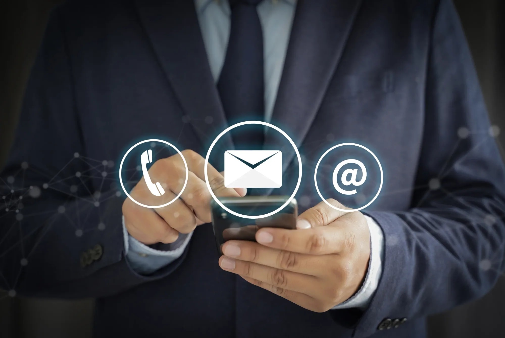 A person in a dark suit holding a mobile phone, with telephone, envelope and at-sign icons in front.