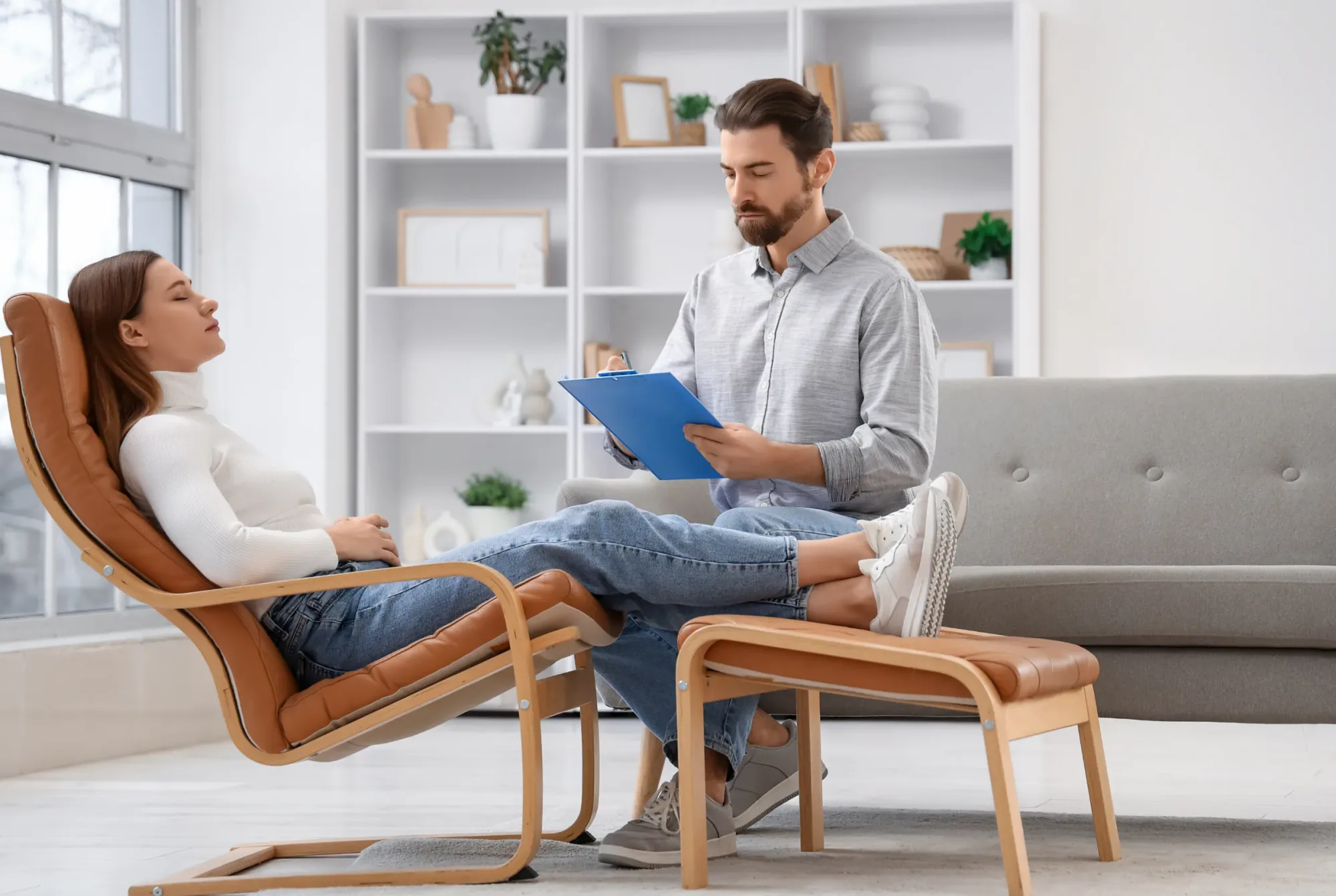 A person resting comfortably in a reclining chair while a practitioner sits nearby with notes during a calm consultation.