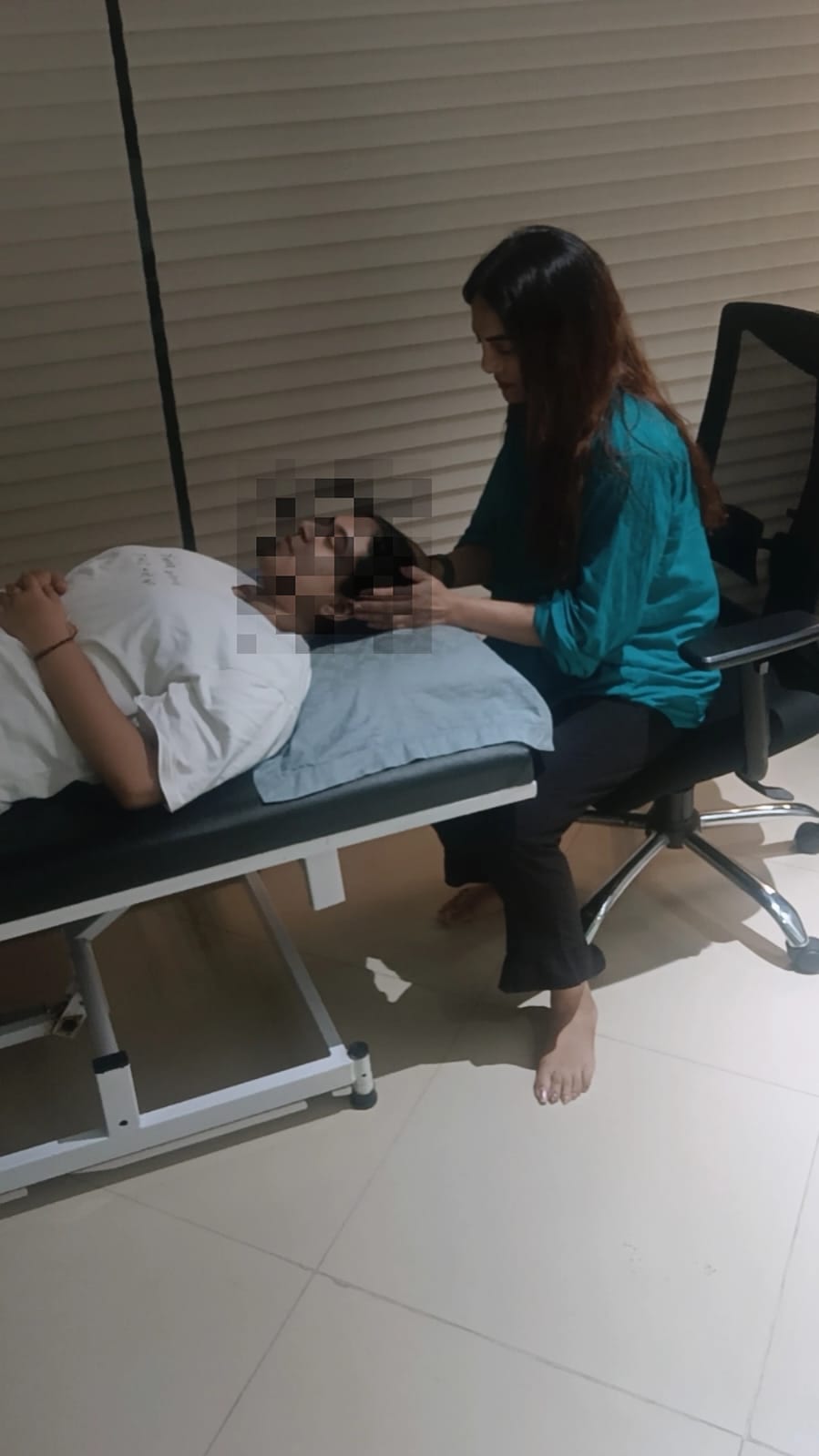 Vibha Jain seated beside a reclining client during a guided session in a quiet treatment room.