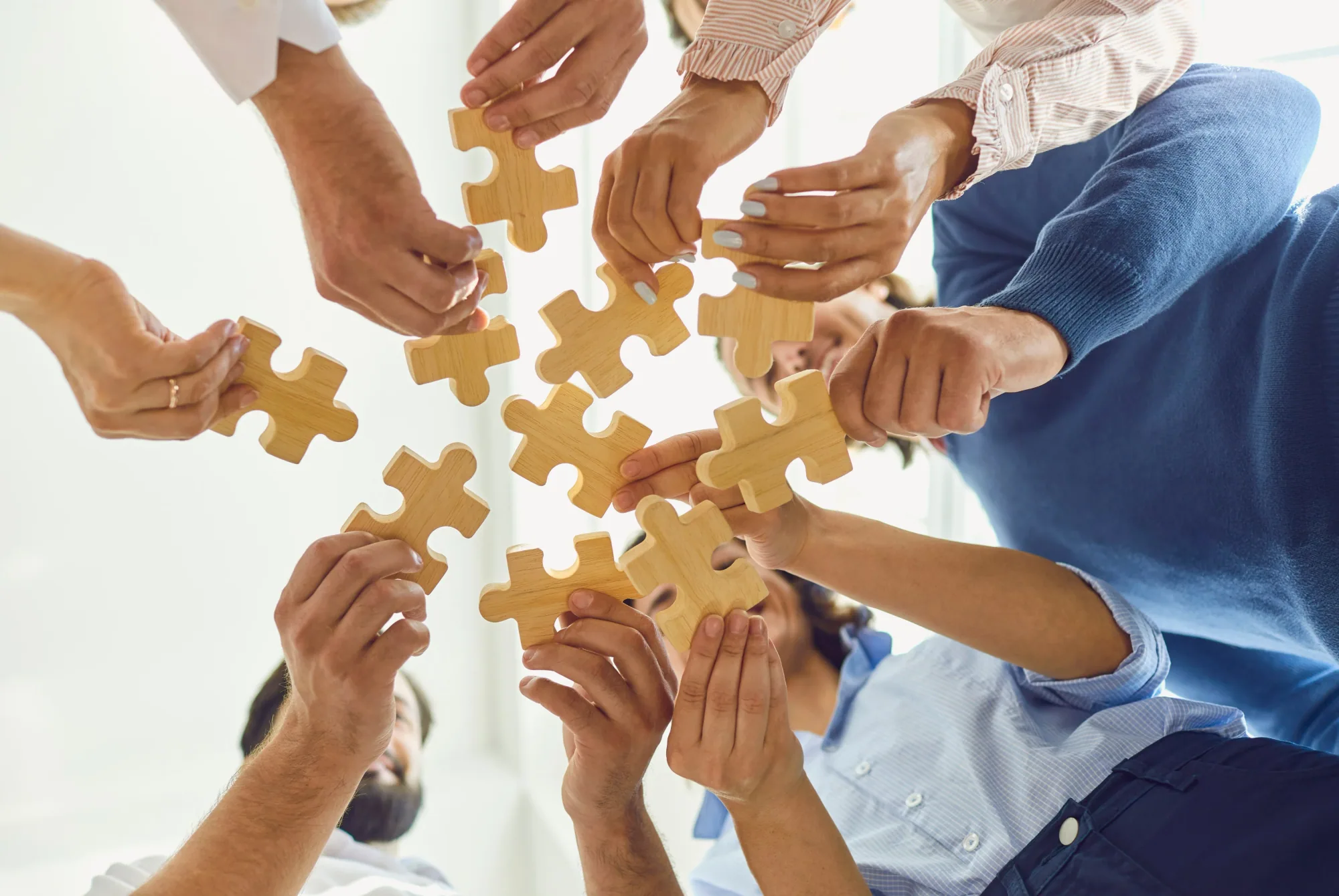A group of people each holding a wooden jigsaw piece towards the centre of a circle.