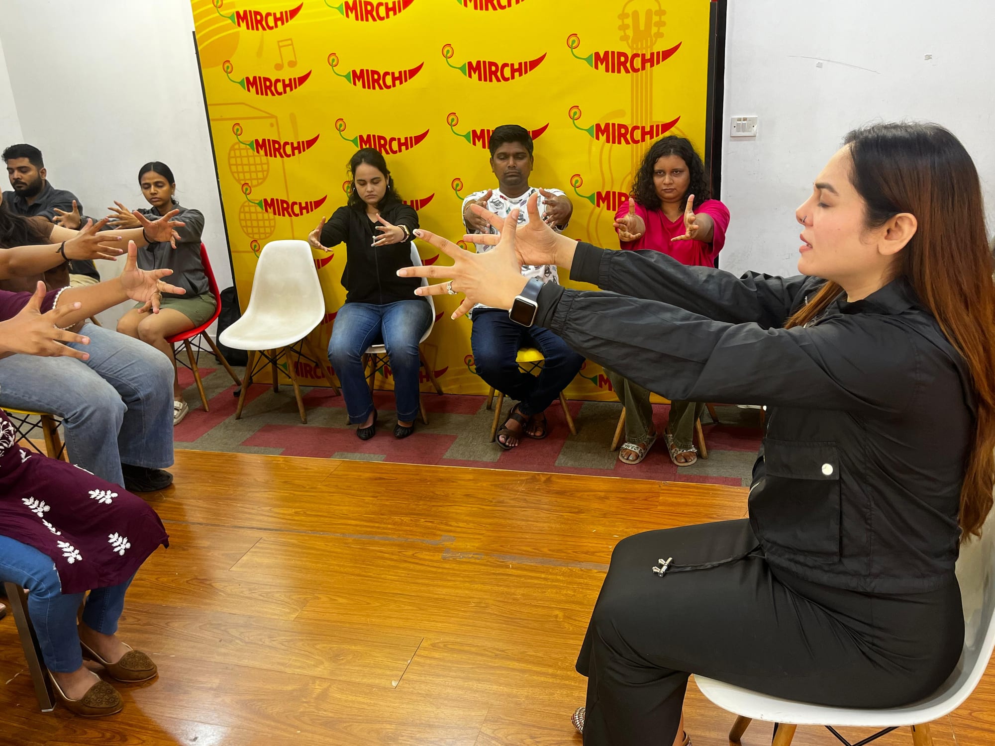 Vibha Jain seated at the front of a room, leading a guided relaxation exercise with a group of seated participants.